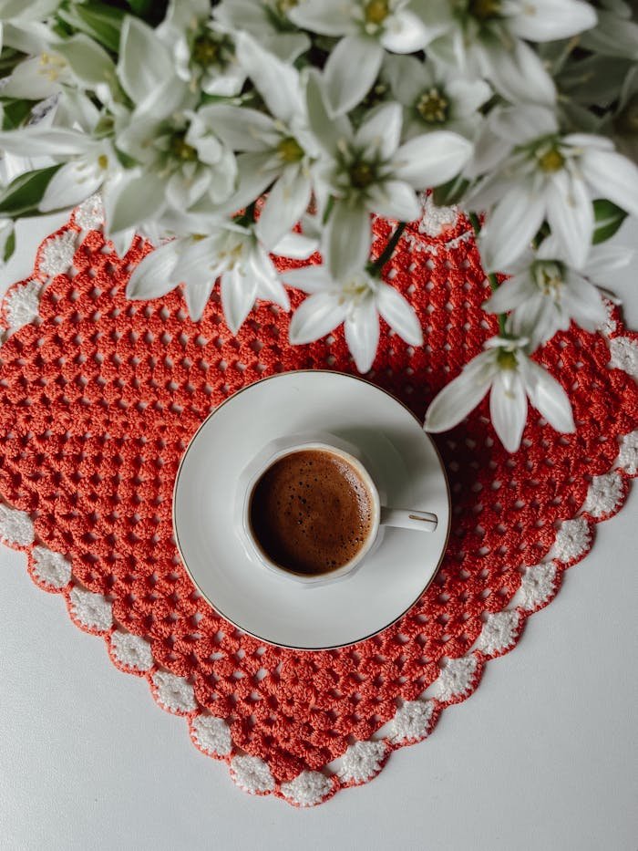 A top view of coffee in a cup with white flowers on a crochet mat.