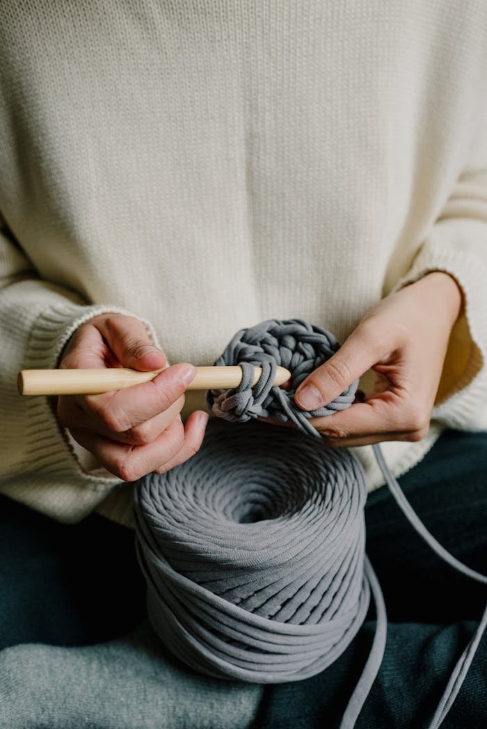 Hands crocheting with gray yarn and a wooden hook, close-up.